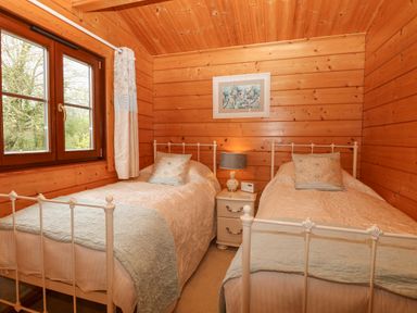 A bedroom with two single beds a nightstand with lamp and radio and a window with curtains at Kingfisher Lodge in Badwell Ash