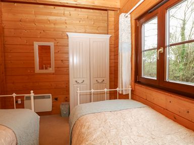A bedroom with two single beds a white wardrobe a wall mirror and a window at Kingfisher Lodge in Badwell Ash