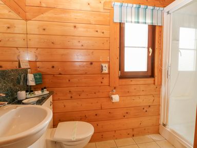 A bathroom with wooden walls a sink a toilet a shower and a window at Kingfisher Lodge in Badwell Ash