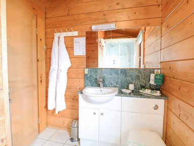 A bathroom with white robes hanging on wall hooks and a sink with toiletries at Kingfisher Lodge in Badwell Ash
