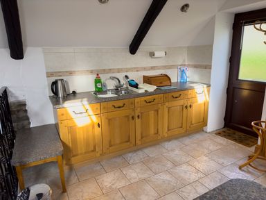 A kitchen with wooden cabinets a sink kettle dish soap and a door at Crogal Stable in New Quay