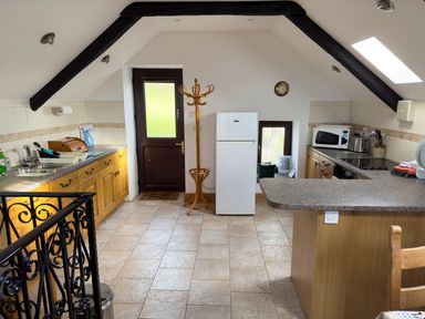 A kitchen with wooden cabinets a white refrigerator a microwave and a coat stand at Crogal Stable in New Quay