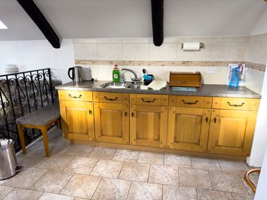 A kitchen countertop with a sink kettle dish soap bread box and cleaning supplies at Crogal Stable in New Quay
