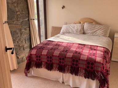 A bed with a red patterned blanket and white pillows next to a stone wall and window at Crogal Stable in New Quay