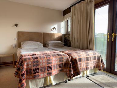 A bedroom with two single beds pushed together covered with patterned blankets next to a window with curtains at Crogal Stable in New Quay