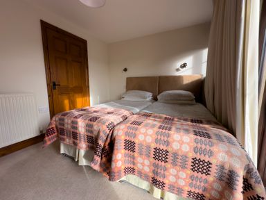 A bedroom with two single beds side by side with patterned blankets and a wooden door at Crogal Stable in New Quay