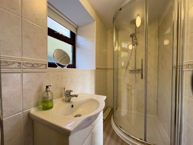 A bathroom with a sink a soap dispenser a round mirror and a glass-enclosed shower at Crogal Stable in New Quay