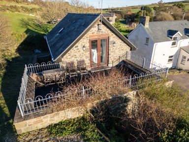 An outdoor terrace with table and chairs in front of a stone house with glass double doors at Crogal Stable in New Quay