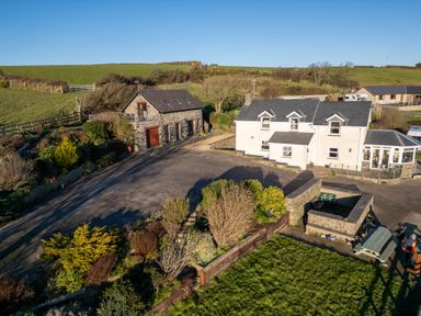 A farmhouse with a stone outbuilding surrounded by gardens and fields at Crogal Stable in New Quay