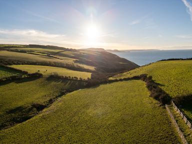 A coastal landscape with green fields hills and the sun shining over the sea at Crogal Stable in New Quay