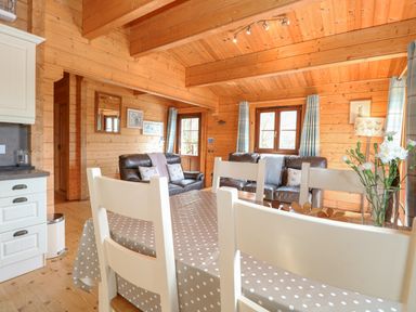 A wooden living room with leather sofas a dining table with white chairs and flowers at Wagtail Lodge in Badwell Ash