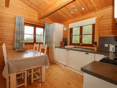 A wooden kitchen with white cabinets table with polka dot tablecloth and four chairs at Wagtail Lodge in Badwell Ash
