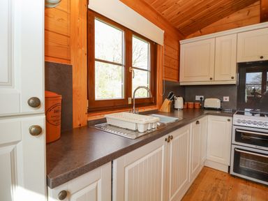 A kitchen with white cabinets a sink a oven a toaster kettle and knife block with wooden walls at Wagtail Lodge in Badwell Ash