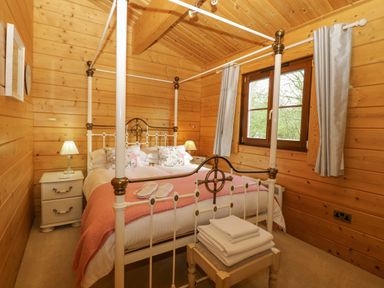 A bedroom with a four poster bed bedside tables lamps a window with curtains and folded towels on a stool at Wagtail Lodge in Badwell Ash