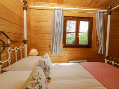 A wooden bedroom with a metal bed frame pillows a lamp and a window at Wagtail Lodge in Badwell Ash