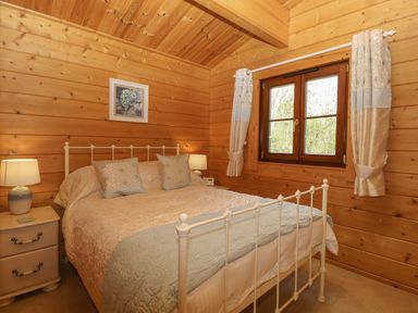 A bedroom with a double bed two bedside tables lamps and a window with curtains at Wagtail Lodge in Badwell Ash