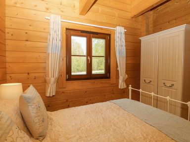 A bedroom with a bed pillows lamp window curtains and a wardrobe at Wagtail Lodge in Badwell Ash