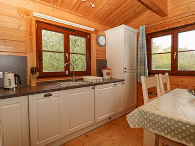 A kitchen with white cabinets a sink a kettle and a table with chairs at Woodpecker Lodge in Badwell Ash