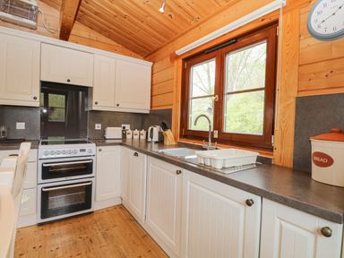 A kitchen with white cabinets a double oven a window above the sink and various kitchen appliances at Woodpecker Lodge in Badwell Ash