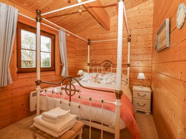 A bedroom with a four-poster bed bedside tables with lamps window and folded towels on a bench at Woodpecker Lodge in Badwell Ash