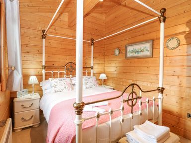 A bedroom with a four-poster bed and wood-paneled walls at Woodpecker Lodge in Badwell Ash