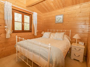 A bedroom with a white metal bed frame bedside table and a window with curtains at Woodpecker Lodge in Badwell Ash