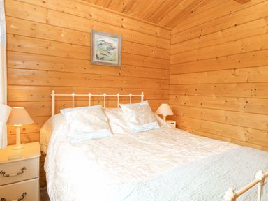 A bedroom with a double bed two bedside tables with lamps and a painting on wooden walls at Woodpecker Lodge in Badwell Ash