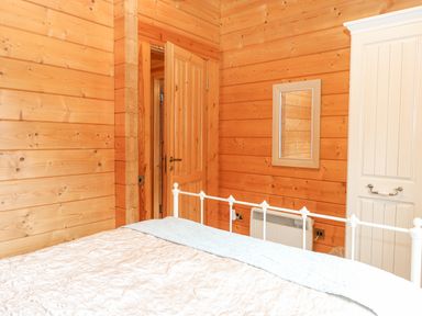 A bedroom with a wooden door a white wardrobe a wall mirror and a white metal bed frame at Woodpecker Lodge in Badwell Ash