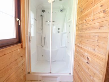 A shower enclosure with a glass door and a handheld shower head in a wooden wall bathroom at Woodpecker Lodge in Badwell Ash