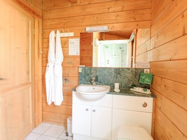 A bathroom with a sink white robes hanging on the wall and wooden paneling at Woodpecker Lodge in Badwell Ash