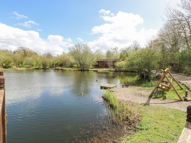 A lake with ducks wooden swing and a cabin surrounded by trees at Woodpecker Lodge in Badwell Ash