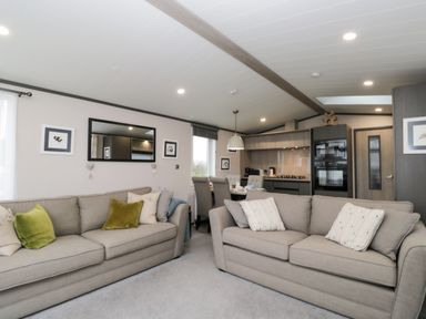 A living room with two beige sofas and a dining area with chairs and kitchen appliances at Tiggywinkles in Chipping Norton