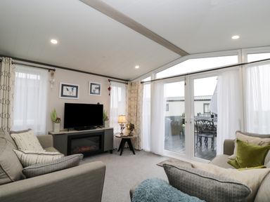 A living room with sofas a television and sliding glass doors leading outside at Tiggywinkles in Chipping Norton