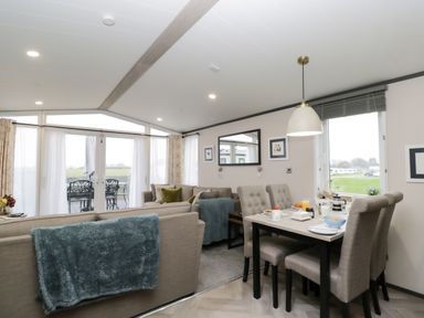 A living room and dining area with beige sofas and a dining table set at Tiggywinkles in Chipping Norton