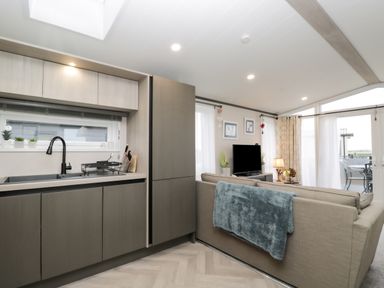 A kitchen with cabinets next to a living room with a sofa and a television at Tiggywinkles in Chipping Norton