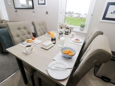 A dining table set with breakfast items including cereal, toast, orange juice, and coffee in a room with beige upholstered chairs at Tiggywinkles in Chipping Norton