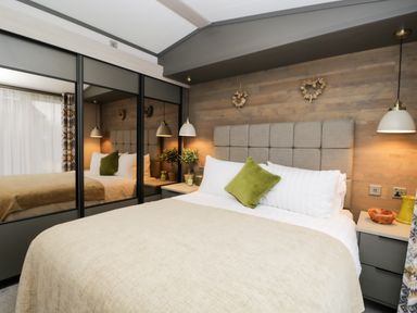 A bedroom with a bed with white and green pillows beside two nightstands and mirrored wardrobes at Tiggywinkles in Chipping Norton