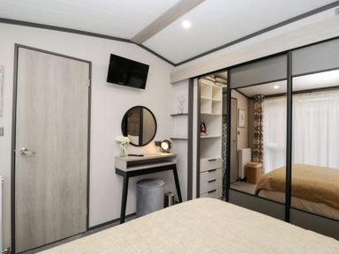 A bedroom with a bed a wall-mounted TV a dressing table with a round mirror and a mirrored wardrobe at Tiggywinkles in Chipping Norton