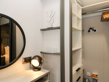 A dressing area with a round mirror a black table lamp a desk shelves hangers and electrical outlets at Tiggywinkles in Chipping Norton