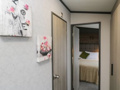 A hallway with two doors and flower artwork on the wall leading to a bedroom with a bed and pillows at Tiggywinkles in Chipping Norton