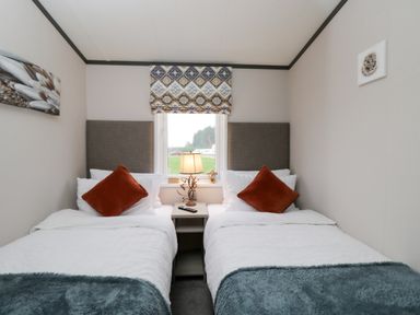 A bedroom with two single beds with orange pillows and a lamp on a bedside table at Tiggywinkles in Chipping Norton