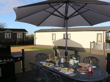 An outdoor dining table with plates of food drinks and flowers under a large umbrella at Tiggywinkles in Chipping Norton