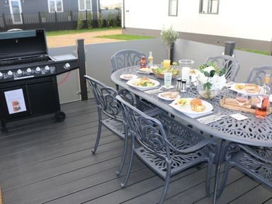 An outdoor dining table with plates of food wine and flowers on a patio next to a barbecue grill at Tiggywinkles in Chipping Norton