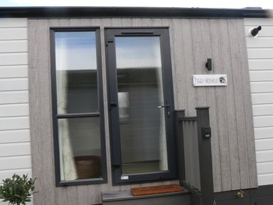 Exterior view of a house entrance with a glass door and window a welcome mat on a small step and a sign reading Tiggy-Winkles on the wall at Tiggywinkles in Chipping Norton