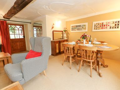 A dining room with a wooden table, four wooden chairs, a patterned armchair with a red pillow, and wall art at The Elbow in Frampton