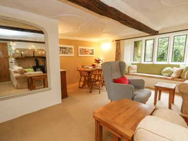 A sitting room with a window seat a checkered armchair wooden tables and a dining table with chairs at The Elbow in Frampton
