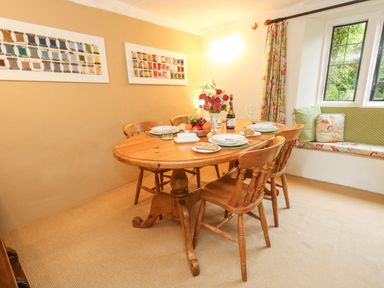 A dining room with a wooden table set for four near a window seat with cushions at The Elbow in Frampton
