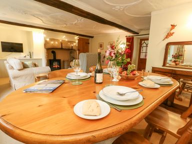 A dining table set with plates glasses and bread near a living area with armchairs and a fireplace at The Elbow in Frampton