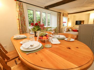A wooden dining table set with plates spoons glasses a bowl of fruit and flowers in a vase by a window in a living room at The Elbow in Frampton