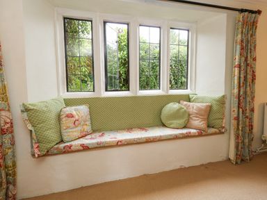 A window seat with cushions and patterned curtains at The Elbow in Frampton